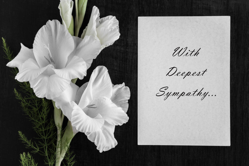 White blank condolence card with text and white gladiolus flower on the dark background.